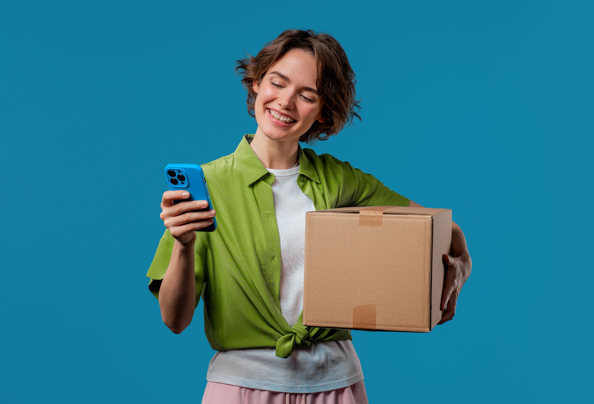 Excited smiling woman, online shopping consumer received cardboard order parcel box, desired purchase. Mobile phone, smartphone mockup with copy space screen for your advertisement
